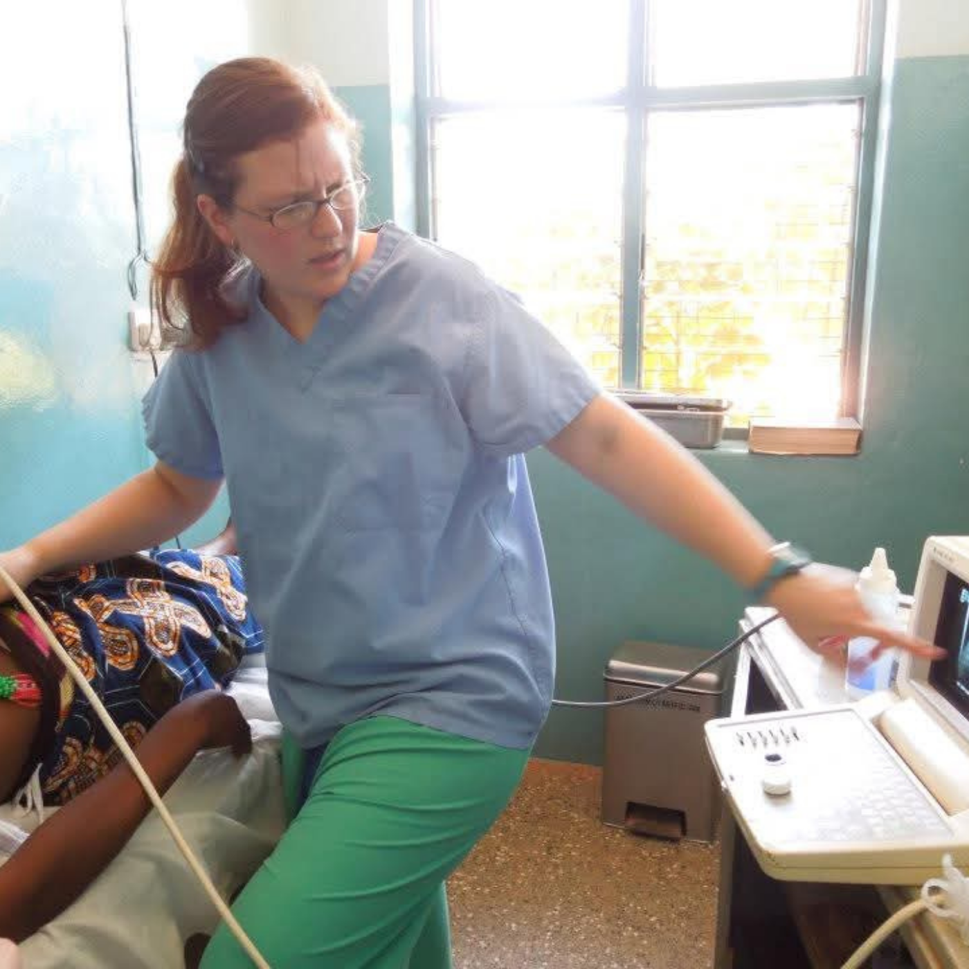 Healthcare volunteer operating an ultrasound machine while examining a patient in a clinic.