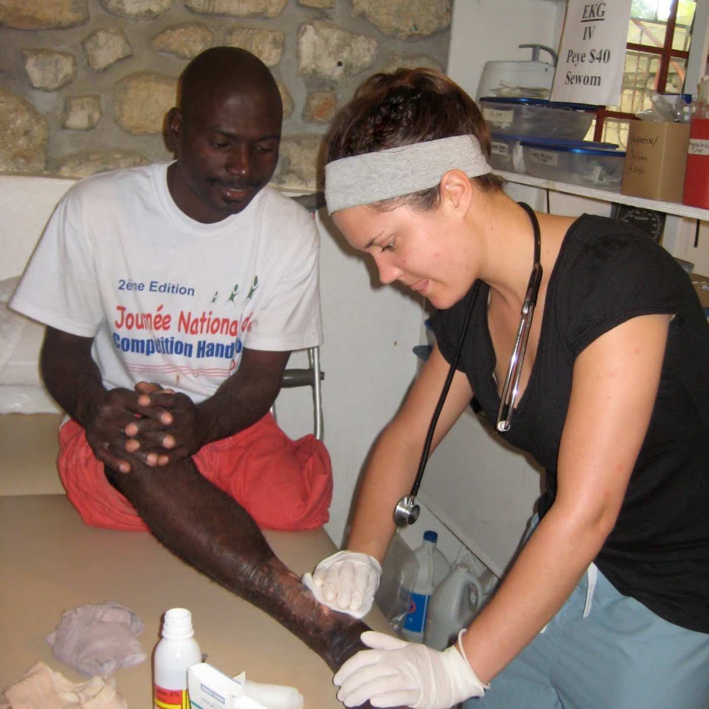 Healthcare volunteer providing wound care treatment to a seated patient.