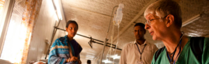 Healthcare professional providing bedside care alongside local clinical staff in a hospital ward.